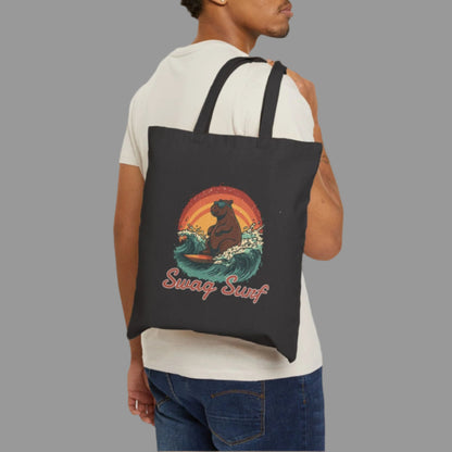 Man carrying a black tote bag with a bear surfing design on a white background