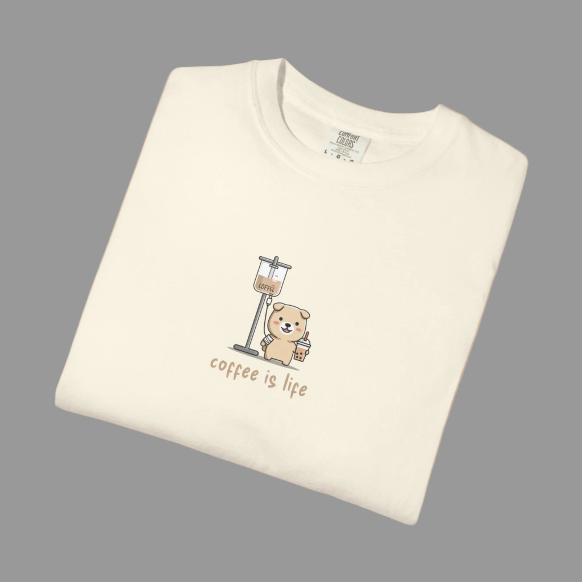 Folded cream-colored t-shirt with a bear and coffee grinder graphic and 'coffee is life' text on a white background.