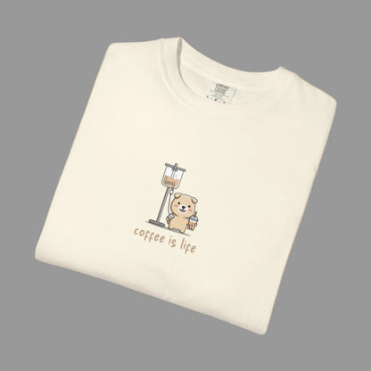 Folded cream-colored t-shirt with a bear and coffee grinder graphic and 'coffee is life' text on a white background.