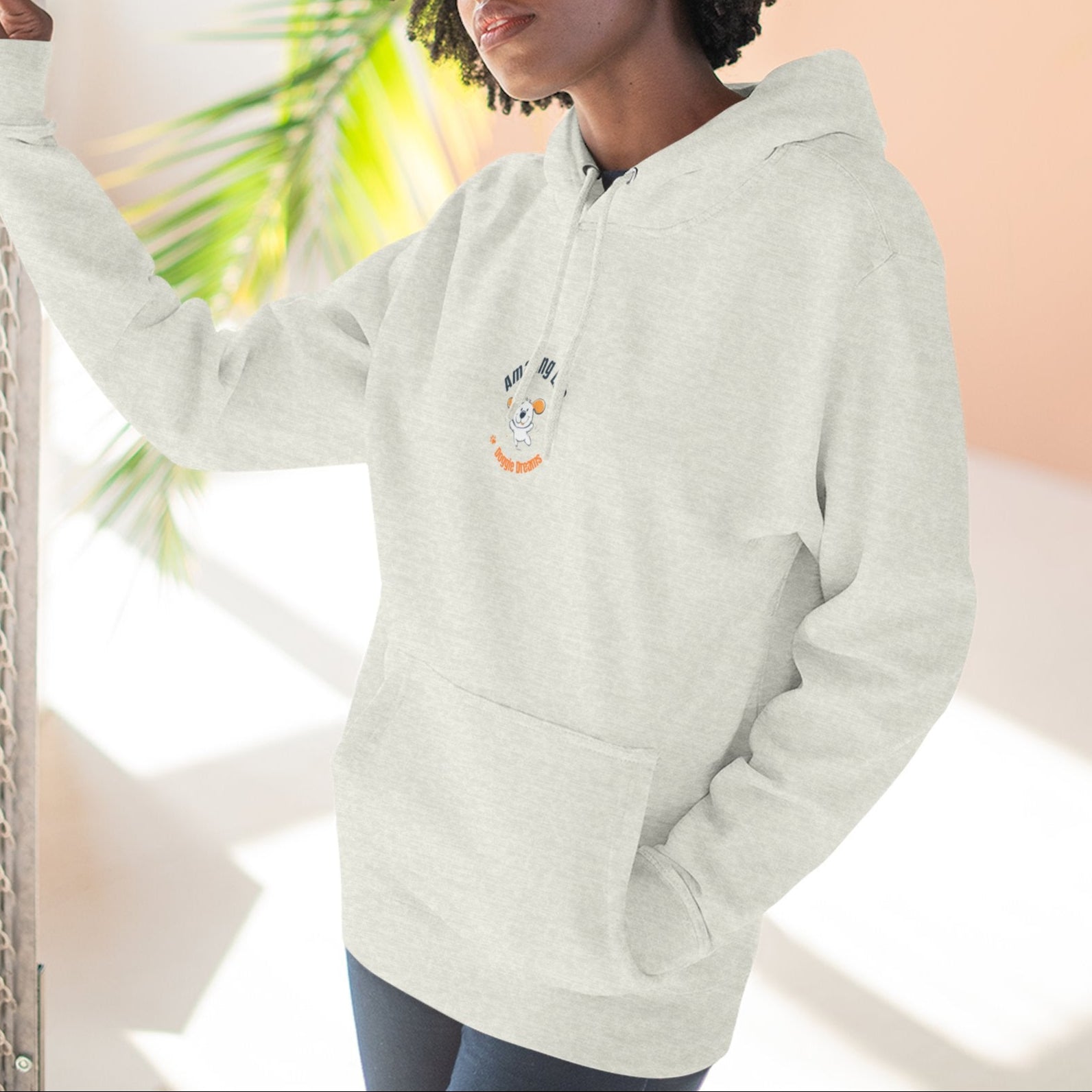 Person wearing a light gray hoodie with a character design, standing against a neutral background with plants.