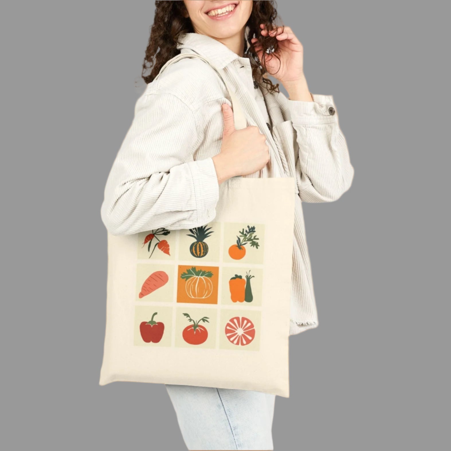 Woman holding a tote bag with fruit and vegetable graphics on a white background