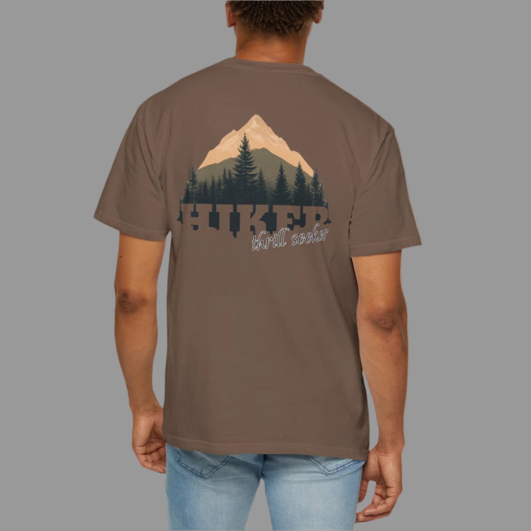 Person wearing a brown t-shirt with a mountain and forest design on the back, on a white background
