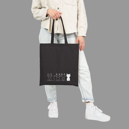 Person holding a black tote bag with cat illustrations on a white background