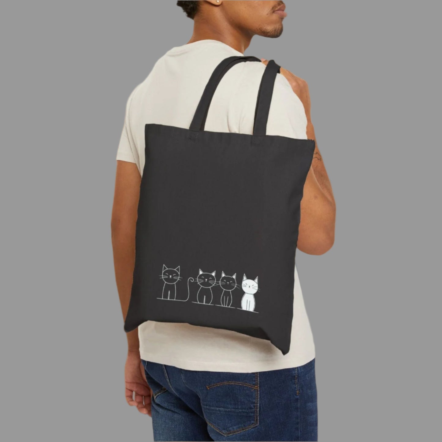 Man carrying a black tote bag with cat illustrations on a white background