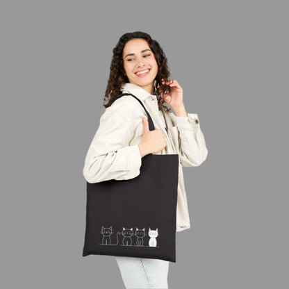 Woman holding a black tote bag with cat illustrations on a white background