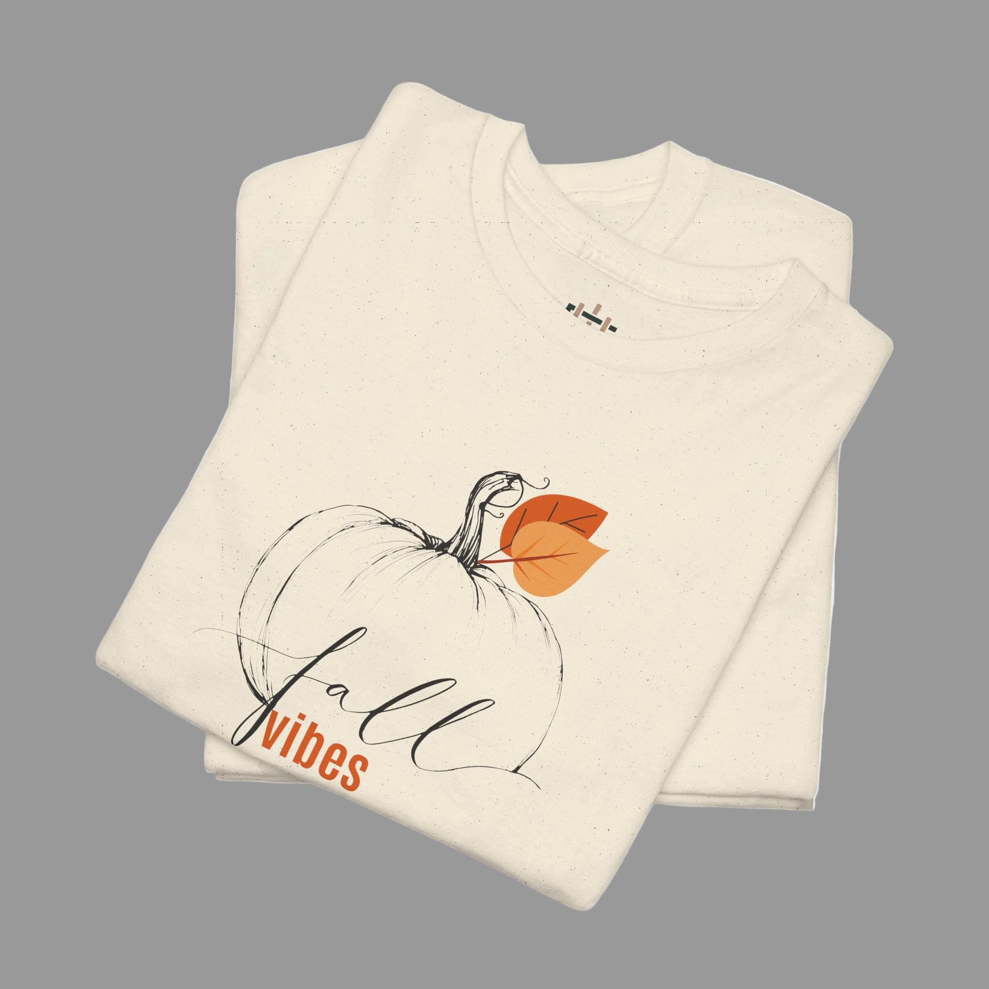 Folded cream-colored shirt with a pumpkin and 'fall vibes' text on a white background