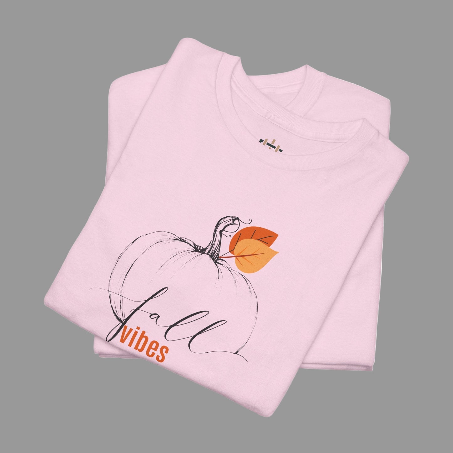 Folded pink t-shirt with a pumpkin and 'fall vibes' text on a white background