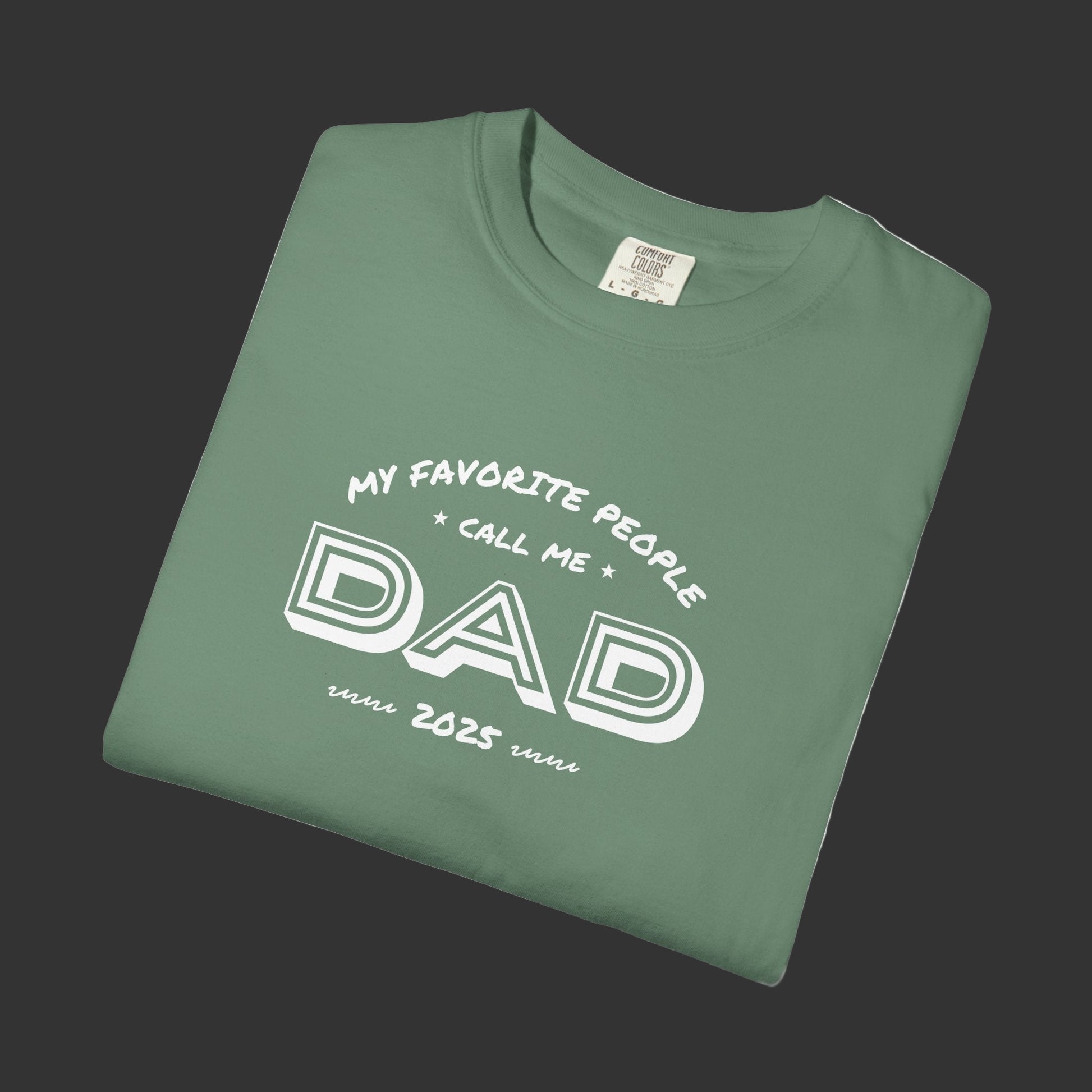 Folded green t-shirt with 'My favorite people call me Dad since 2023' text on a white background