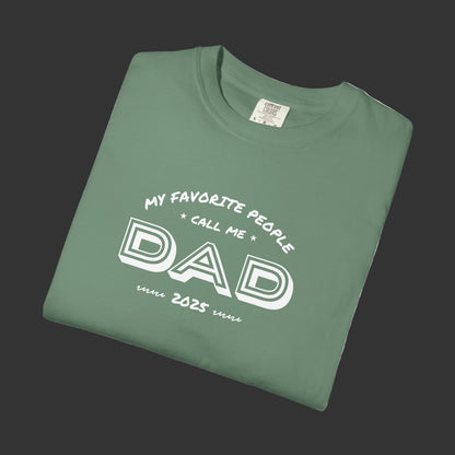 Folded green t-shirt with 'My favorite people call me Dad since 2023' text on a white background