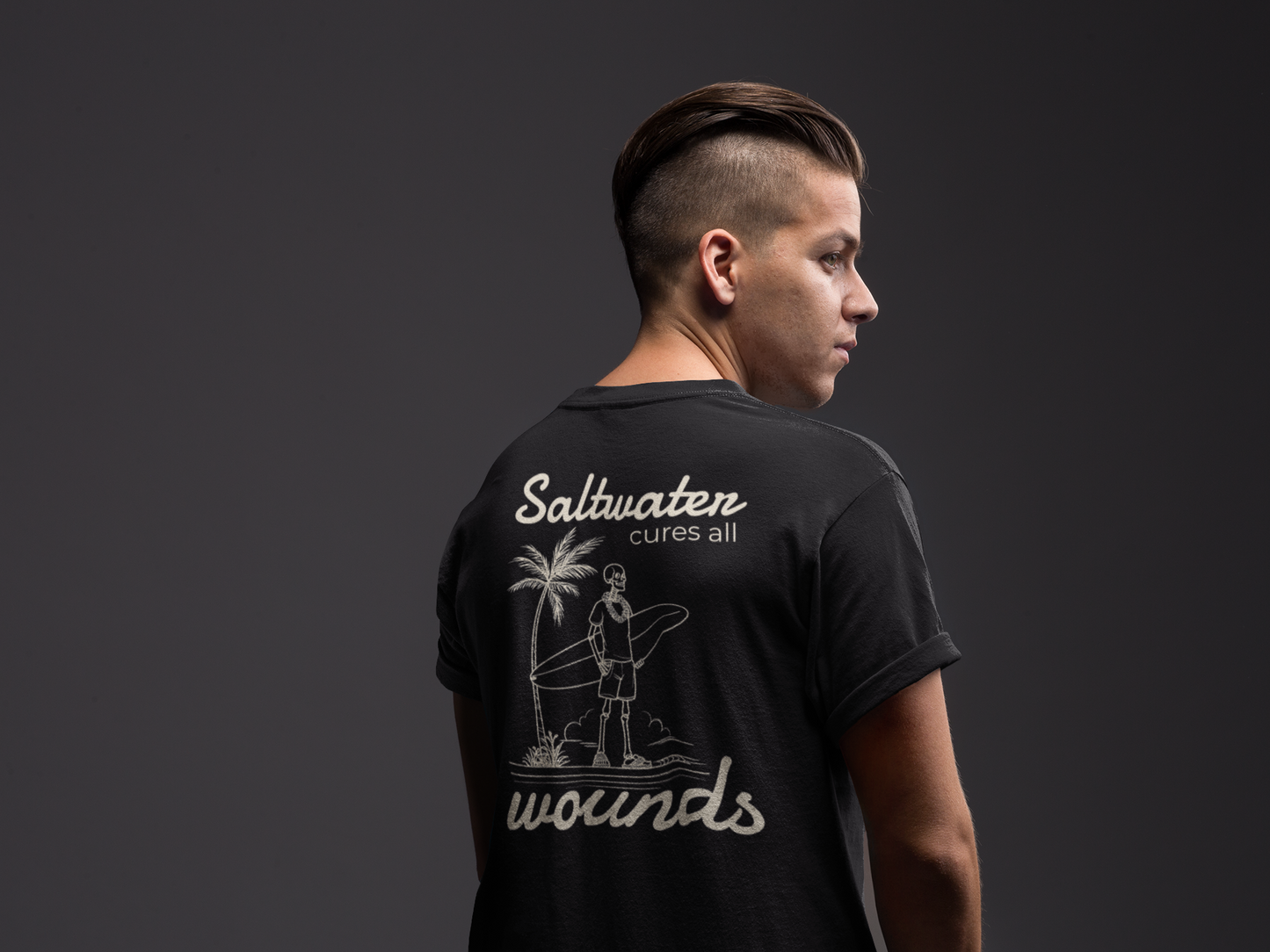 Person wearing a black t-shirt with 'Saltwater cures all wounds' text and graphic on the back against a dark background