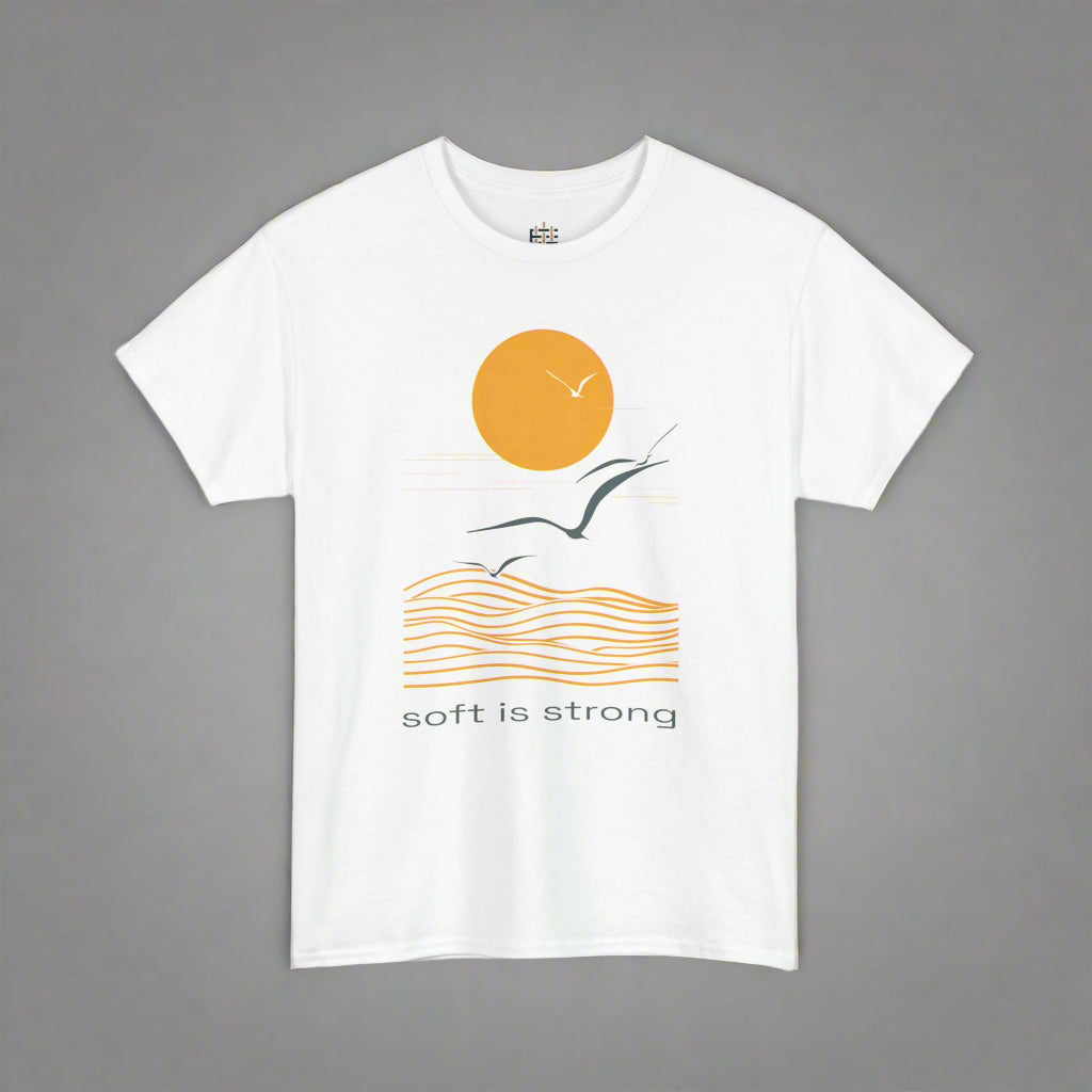 White t-shirt with a graphic design of a sun, wave, and bird, with 'soft is strong' text on a white background.