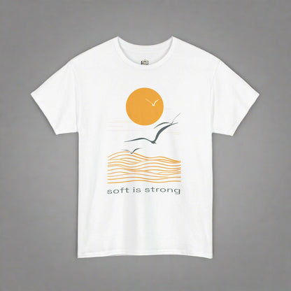 White t-shirt with a graphic design of a sun, wave, and bird, with 'soft is strong' text on a white background.