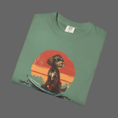 Folded green t-shirt with a dog on a surfboard graphic against an orange sunset background