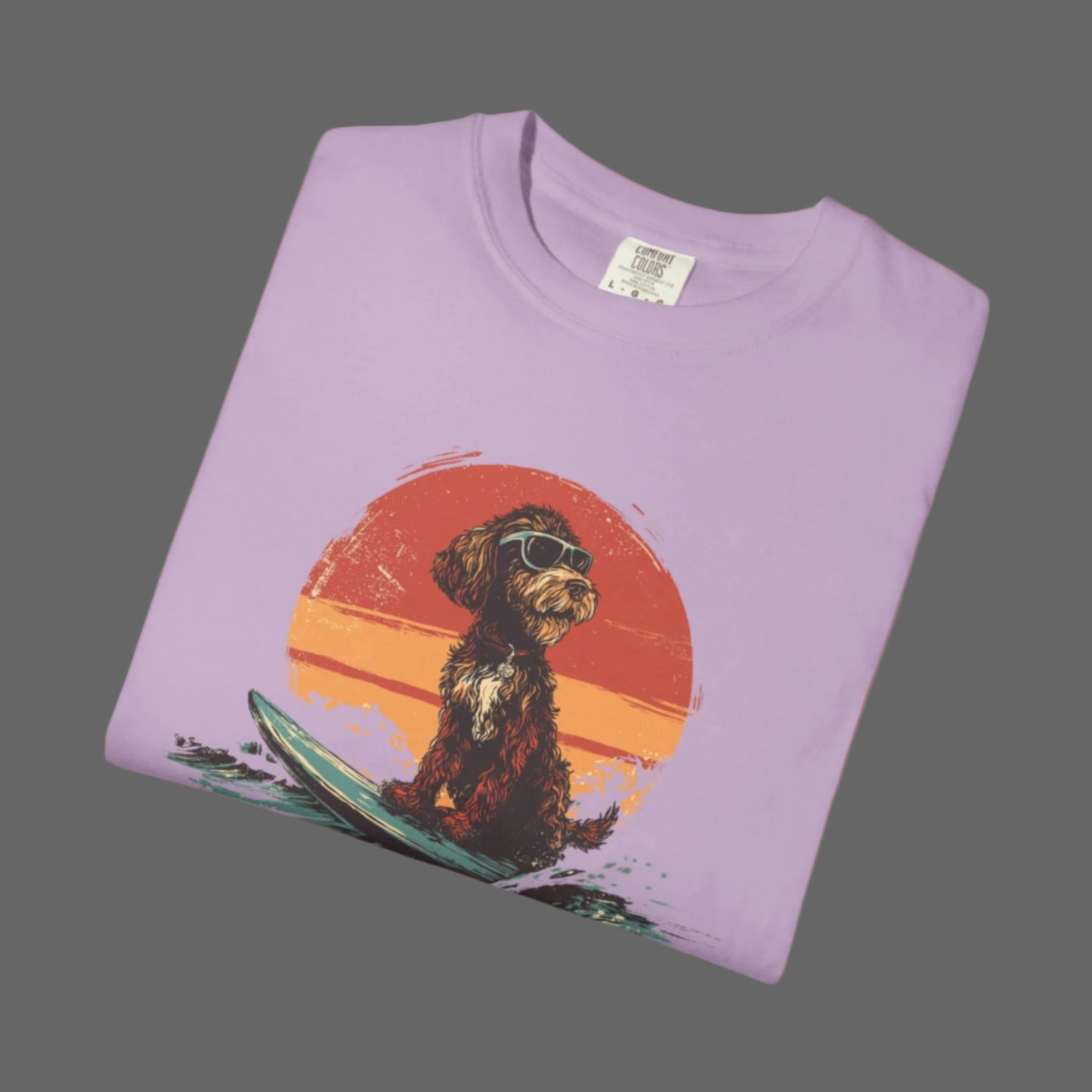 Folded purple t-shirt with a dog on a surfboard graphic against a sunset background