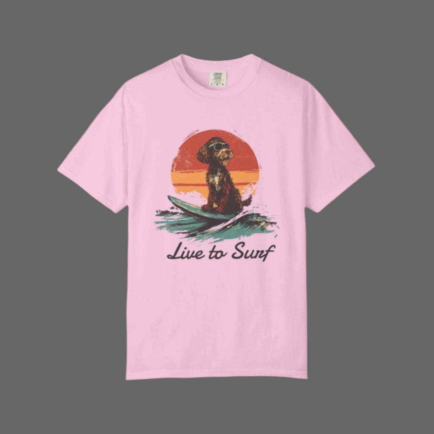 Pink t-shirt with a graphic of a dog on a surfboard and 'Live to Surf' text, on a white background.