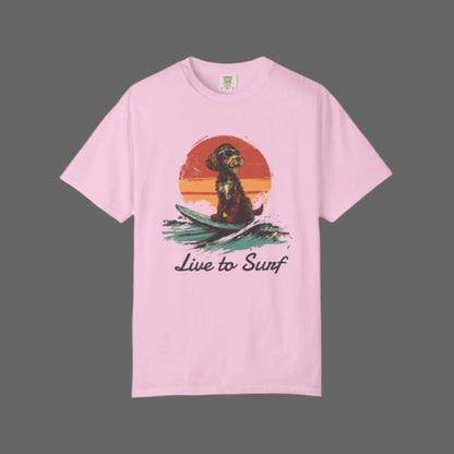 Pink t-shirt with a graphic of a dog on a surfboard and 'Live to Surf' text, on a white background.