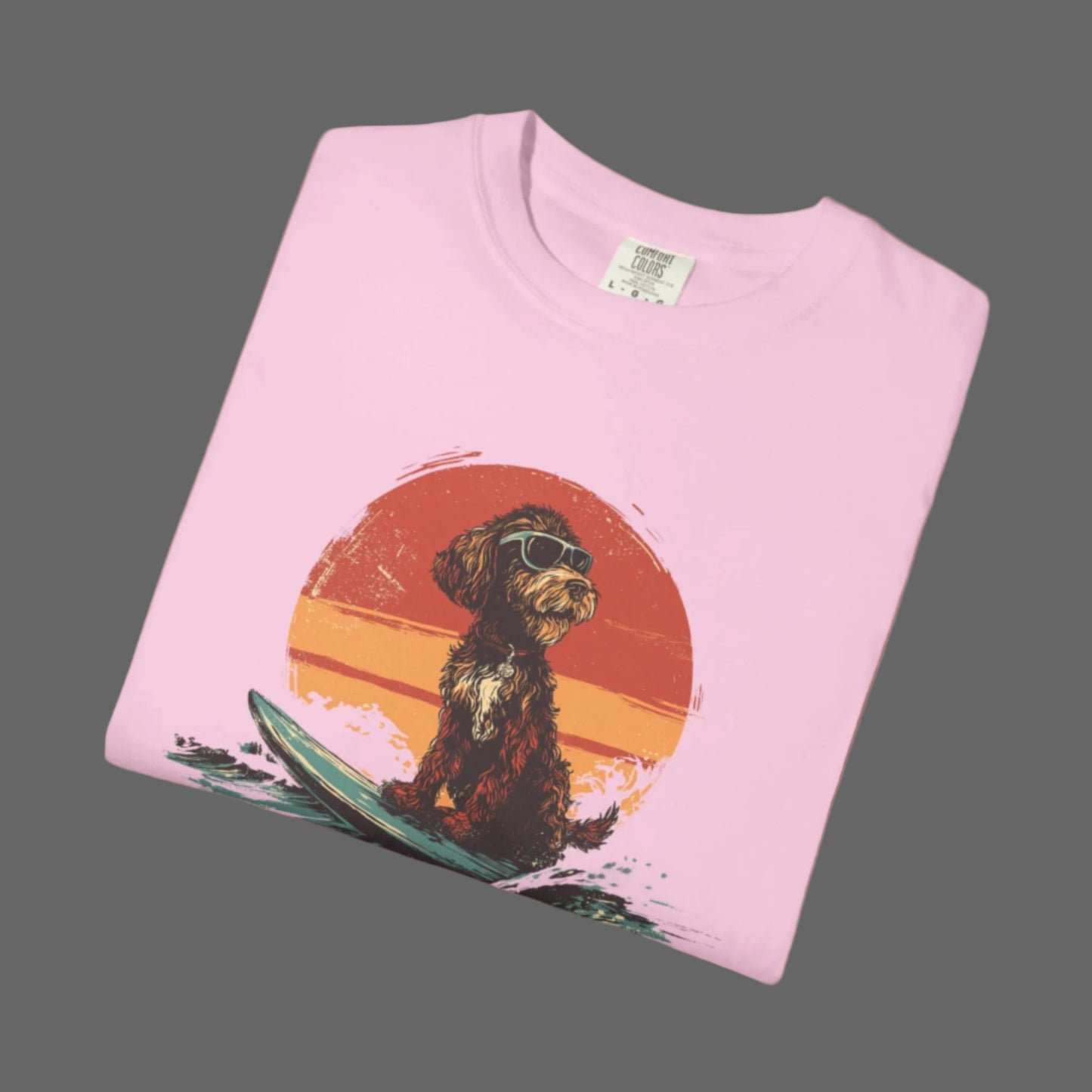 Folded pink t-shirt with a dog on a surfboard graphic on a white background