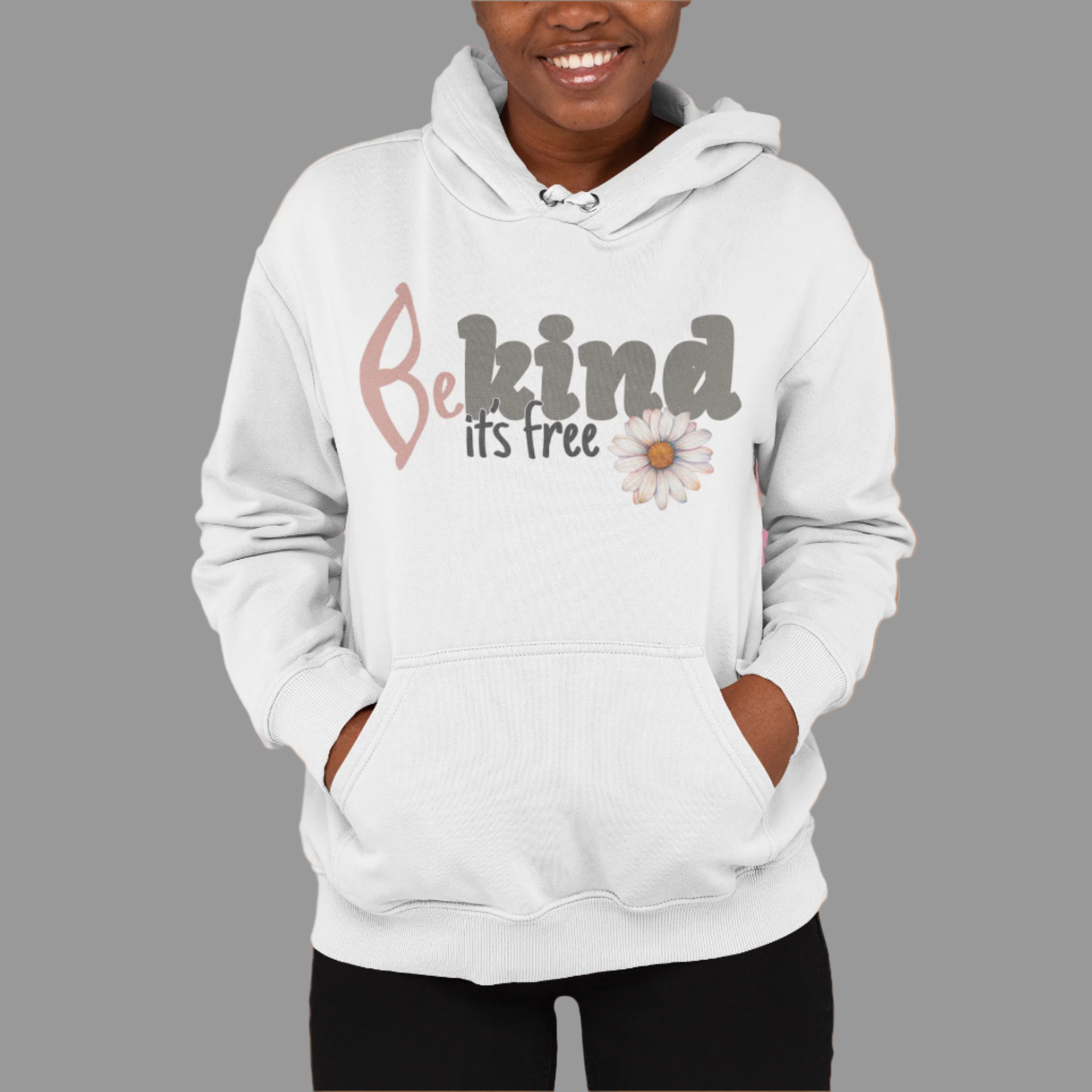 A woman smiling, wearing a white hoodie with the text 'BE KIND IT'S FREE' and a floral design on the front.